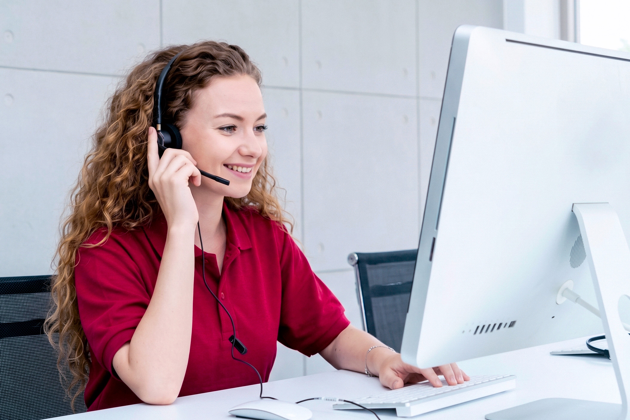 Woman in Novoffice customer service wearing a headset with microphone, smiling in front of a computer screen at her desk.