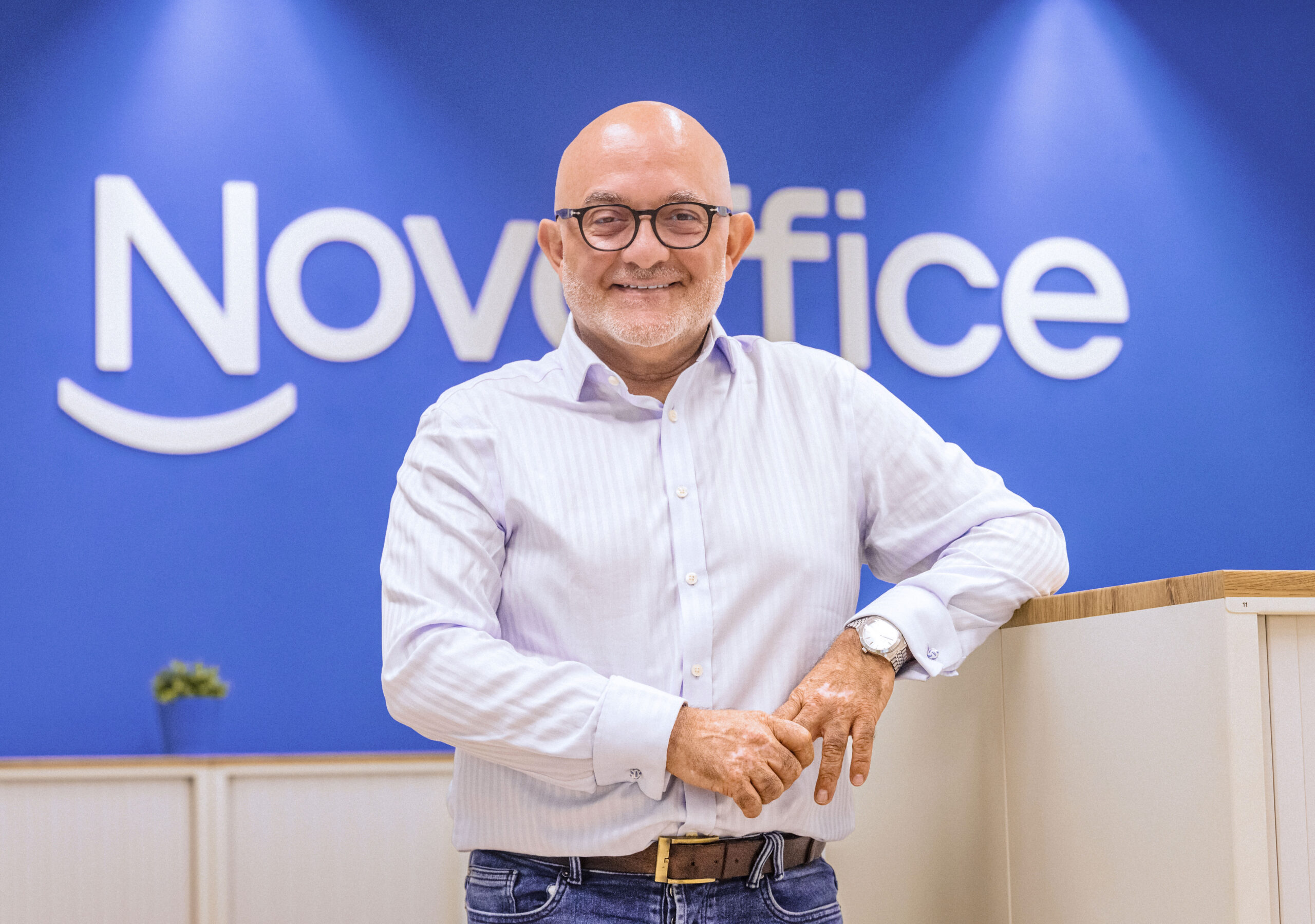 Giuseppe Albicocco — Novoffice team member posing in front of the brand's blue logo in the company's offices.