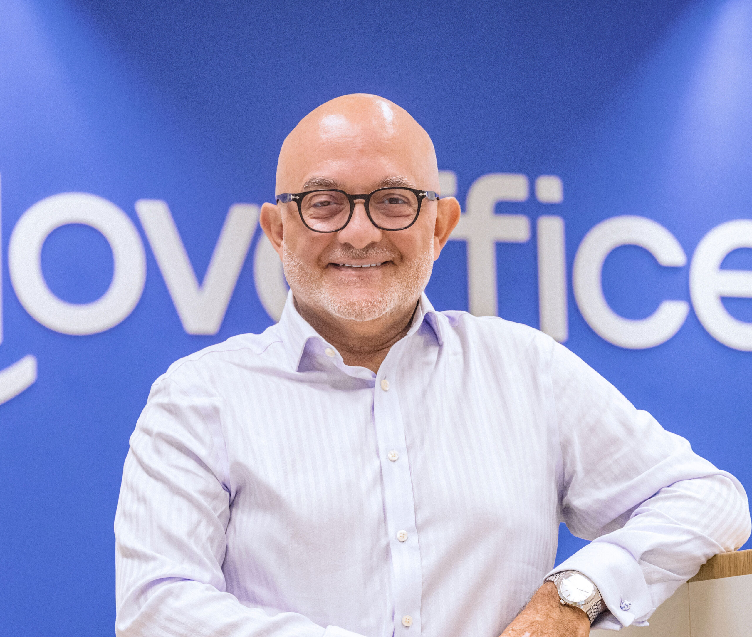Giuseppe Albicocco — Novoffice team member posing in front of the brand logo, wearing a lavender shirt.